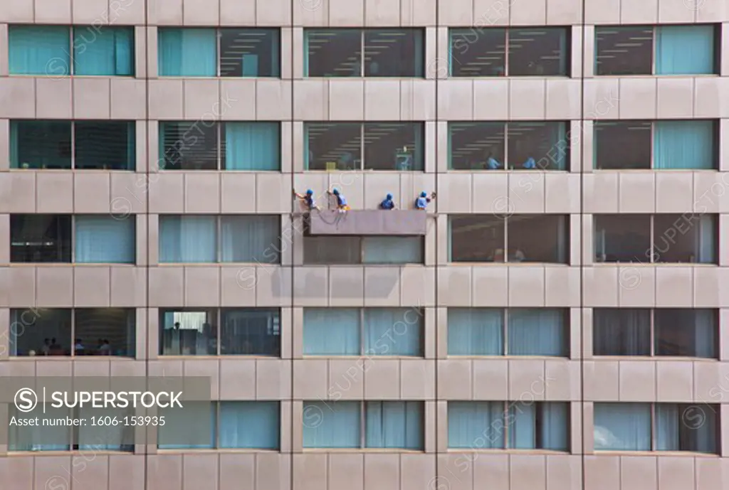 A cleaning crew hang suspended on the side of a highrise office building while businessmen work inside, located in the Akasaka district of central Tokyo, japan.