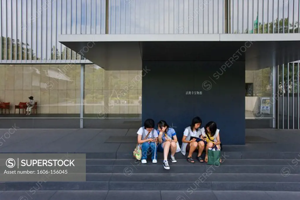 Young Japanese girls consult their cellphones on the steps of the Gallery of Horyuji Treasures at the Tokyo National Museum, located inside Ueno Park in the old shitamachi downtown Ueno district of Tokyo, japan.