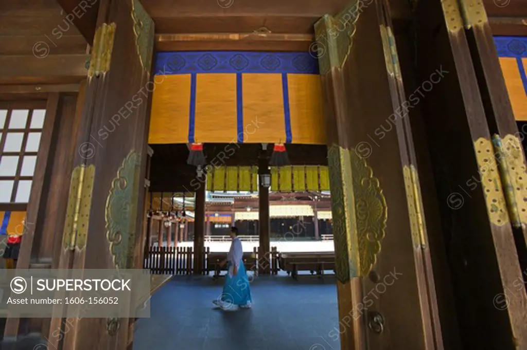 A kannushi Shinto priest walks by the row of great wooden doors with decorative metalwork at the Outer Shrine of Meiji-Jingu Shrine, located in the Shibuya district of Tokyo, Japan.