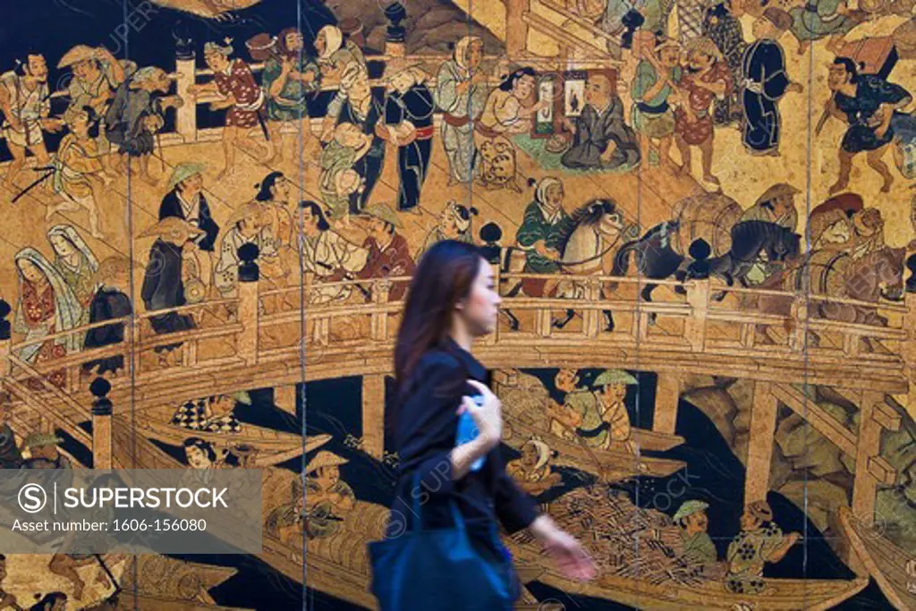 A young Japanese woman rushes by an old Edo-era woodblock print of the venerable Nihonbashi Bridge, which is being used as a mural for a construction site wall in the Nihonbashi district of central Tokyo, Japan.