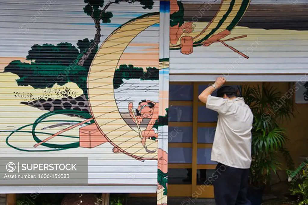 The owner opens the shutters of his traditional Japanese restaurant that are decorated with a Hokusai woodblock print in the Nihonbashi district of central Tokyo, Japan.