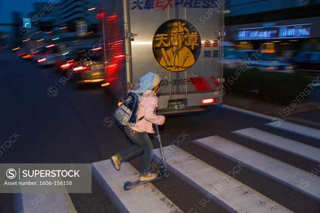 A young Japanese girl zips across Aoyama Dori Avenue on her Razor Skateboard at twilight in the fashionable Aoyama district of central Tokyo, Japan.