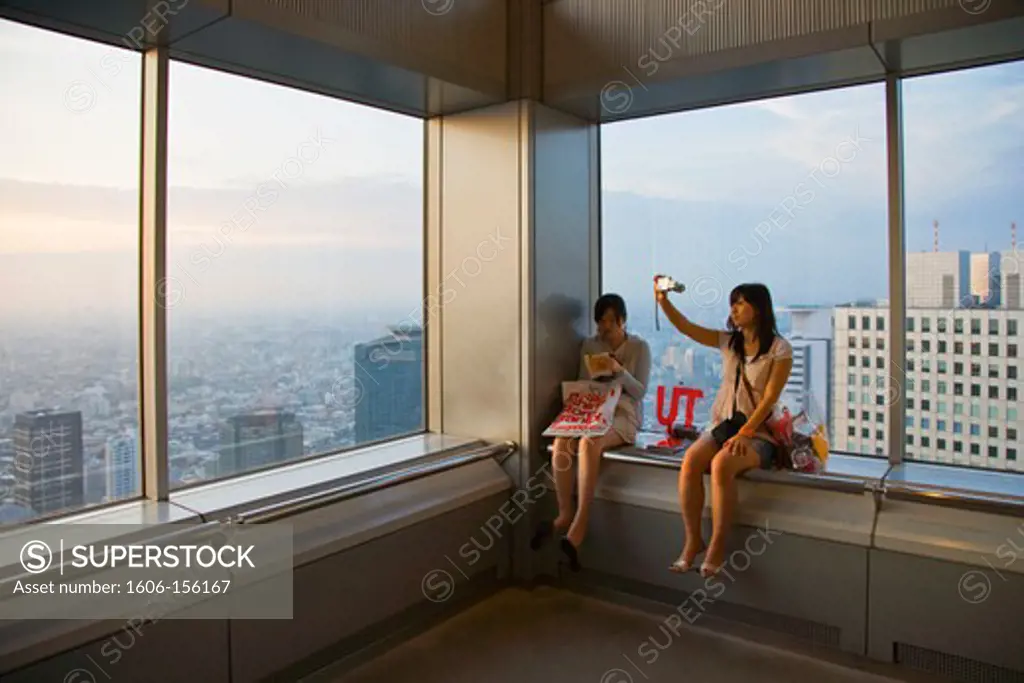 Two young Japanese women relax at twilight in the public observatory atop the twin towers of the Tokyo Metropolitan Government Center in the Shinjuku District of Tokyo, Japan.