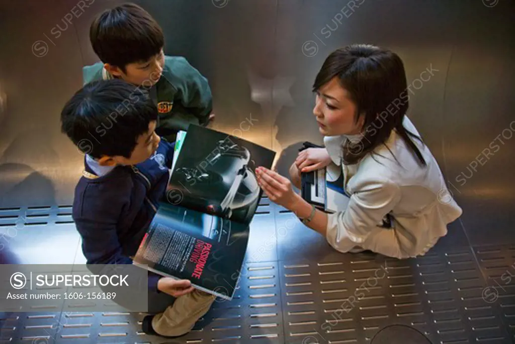 A young female staff member chats with potential future customers, 2 young Japanese boys, at the Nissan Auto Showroom in the center of the Ginza District in Tokyo, Japan.