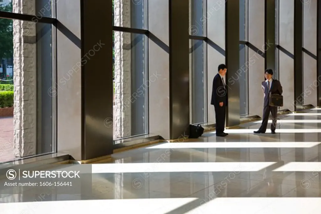 Japanese businessmen meet in the sunny lobby of the Shinjuku Center Building in the early morning in the highrise district of West Shinjuku in Tokyo, Japan.