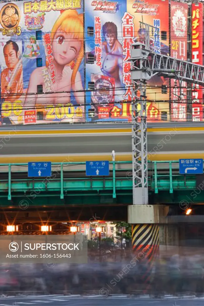 A morning rush of workers with commuter trains overhead cross Yasukuni Dori Avenue with Kabukicho District building-size posters as backdrop at Shinjuku Station in Tokyo, Japan.