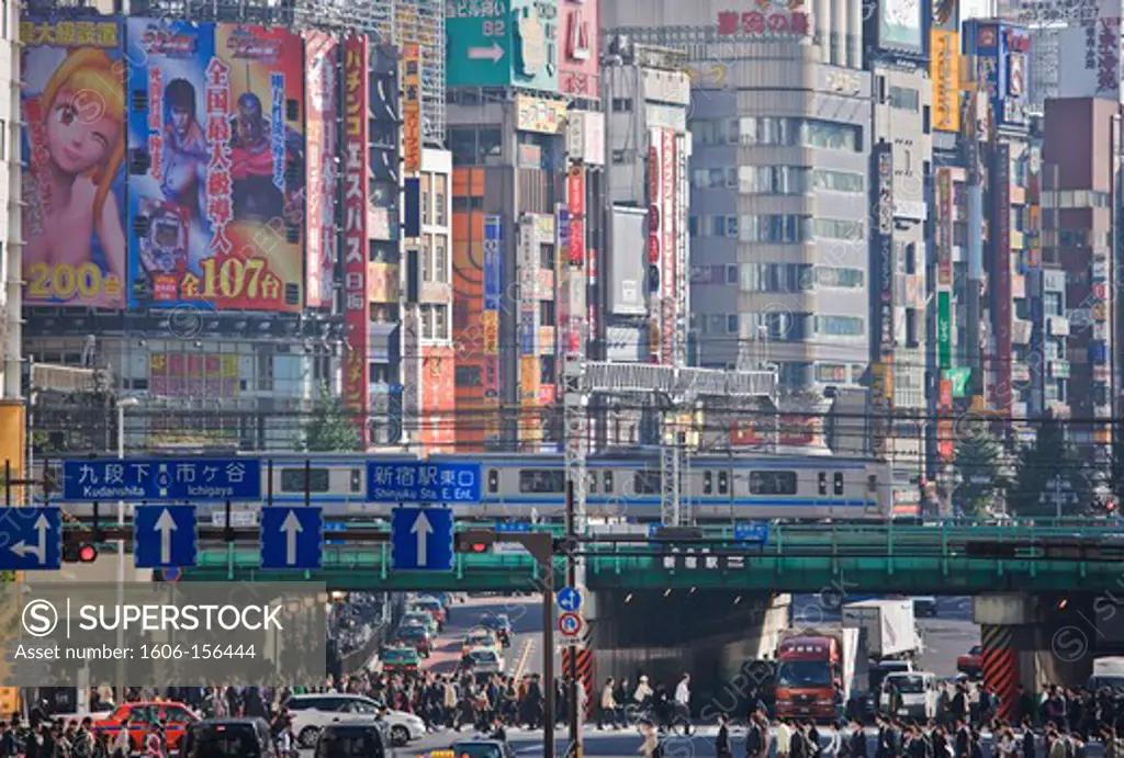 A morning rush of workers with commuter trains overhead cross Yasukuni Dori Avenue with Kabukicho District building-size posters as backdrop near Shinjuku Station in Tokyo, Japan.