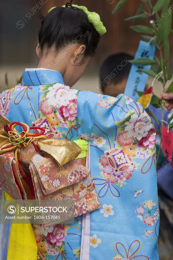 A detailed view shows the traditional kimono of a young girl visiting Kitano Tenmangu Shrine in Kyoto, Japan.
