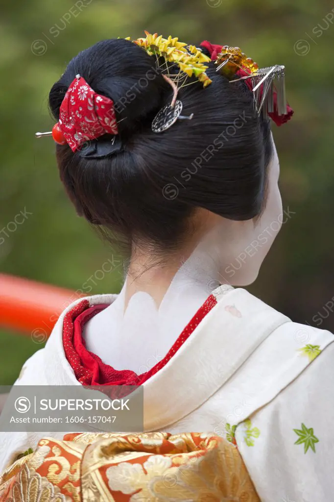 A maiko geisha walks along the Kamiya River at Kitano Tenmangu Shrine in Kyoto, Japan.