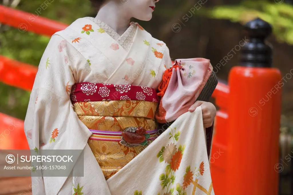 A maiko geisha walks along the Kamiya River at Kitano Tenmangu Shrine in Kyoto, Japan.
