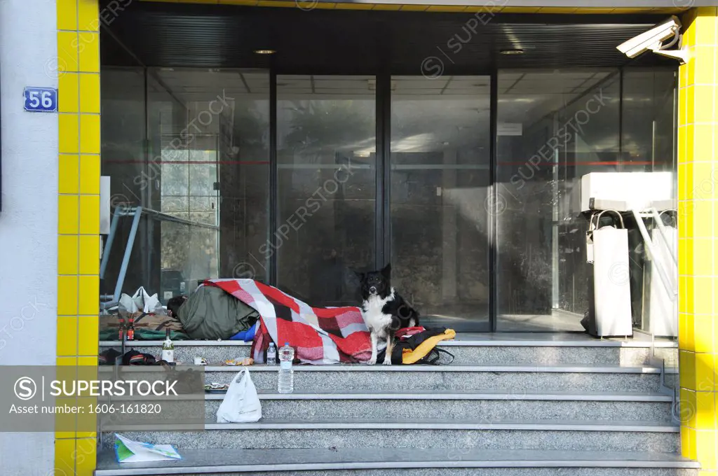 France, (01/2009) 44, Nantes. Homeless in a sleeping bag and under blankets in winter lay next to his dog at the entrance of a building, surveillance camera.