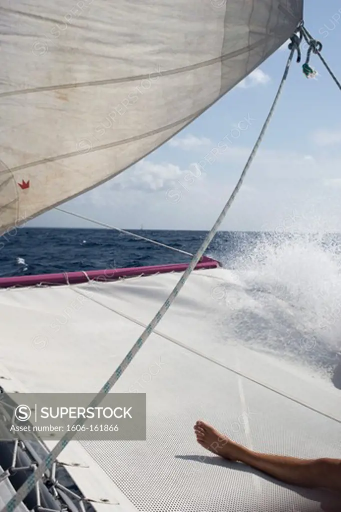 Catamaran 's sail and spindrift, trampoline and man's leg laying, Mauritius, Indian Ocean