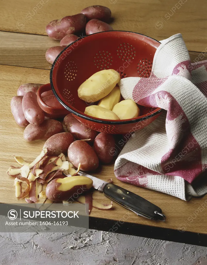 Pink potatoes on a table and in a red sieve, cloth, knife