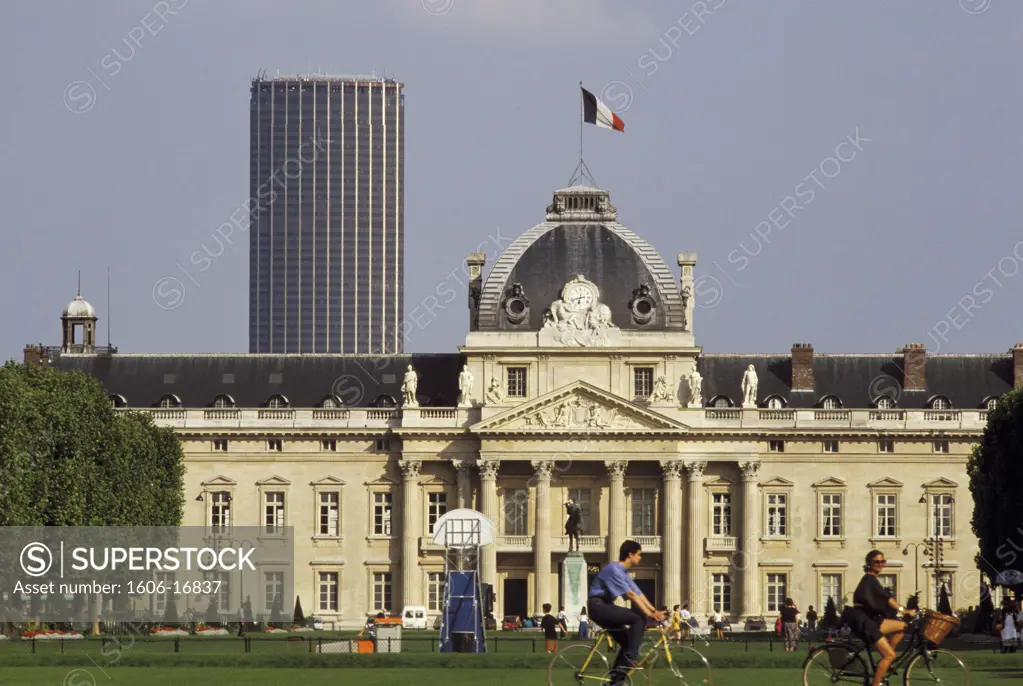 France, Paris, façade of Military Academy, Champ de Mars, couple biking, lawn, Montparnasse tower at the back, summer, sky