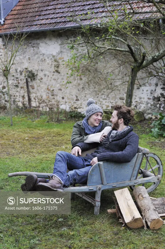 Young couple outside with wheelbarrow and firewood