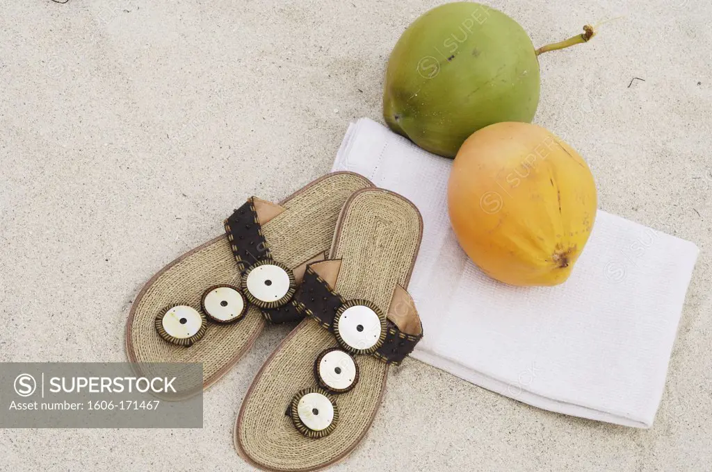 Pair of tongs on white sand and coconut