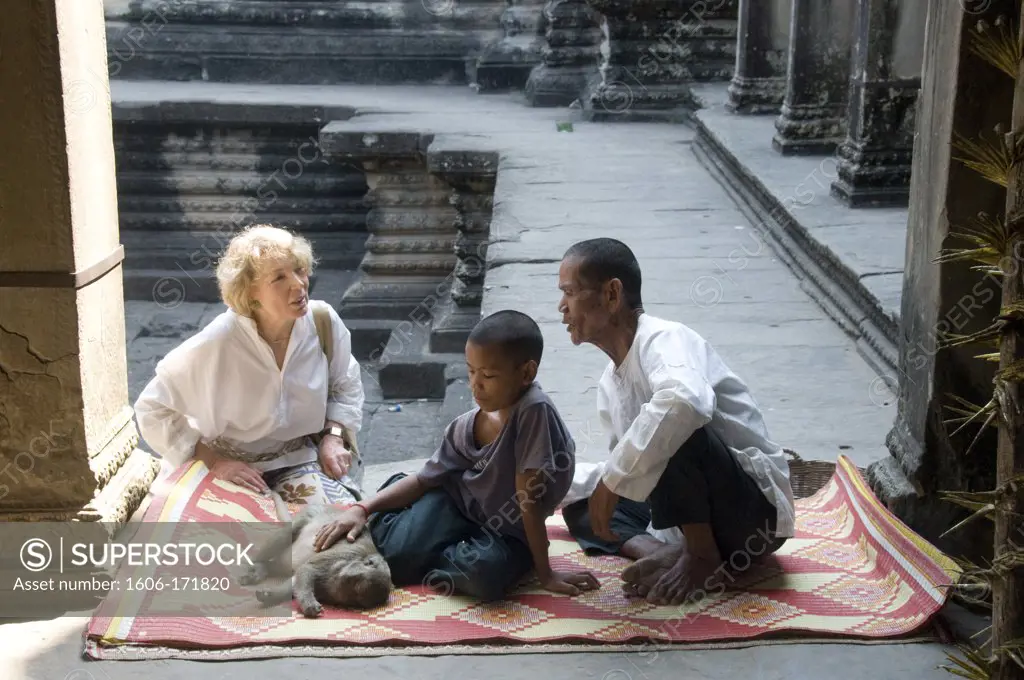 Asia, Cambodia,  Siem Reap , Angkor Wat, woman tourist with father his son and monkey seated on a carpet in courtyard of temple.
