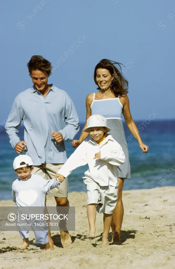Couple and two little boys running on a beach, smiling, sea in background, blue sky