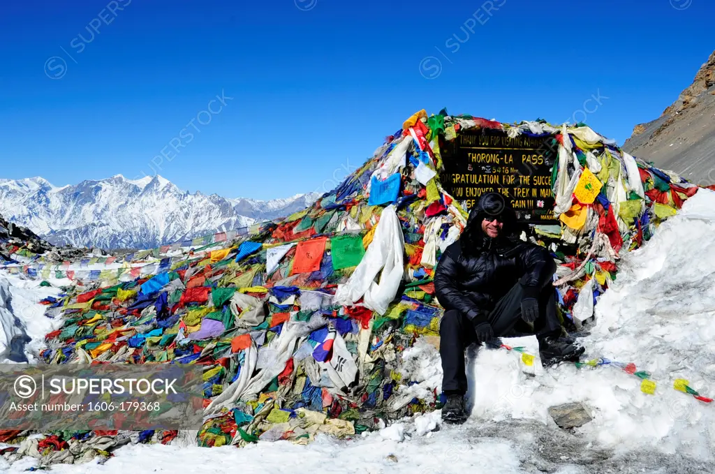 Nepal Annapurna ring man wearing a down jacket seating in front of the THORONG LA pass sign covered by prayers'flags at 5400m high