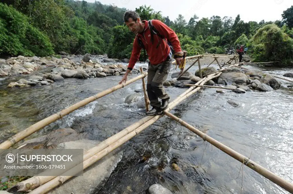Burma, Myanmar, PUTAO area a european man is crossing a river on a bamboo bridge