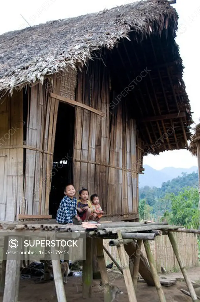 Burma, Myanmar, PUTAO area 3 kids are sitting down in front of their traditional bambou house