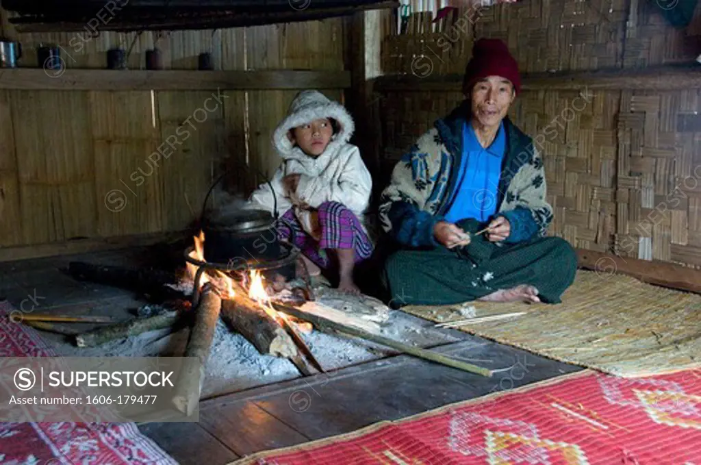Burma, Myanmar, Putao, a grand father and his grand daughter are sitting around a fire place inside their bamboo hut