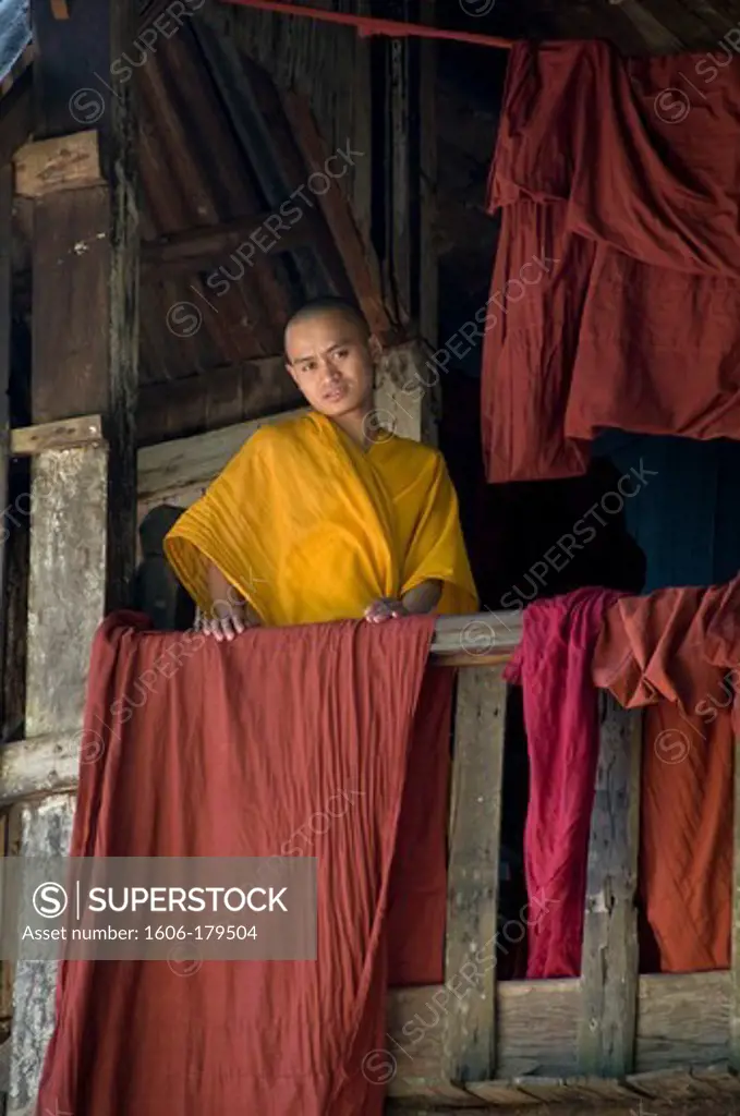 Myanmar Burma BAGO a monk wearing a yellow toga is leaning against a fence where red fabrics are drying