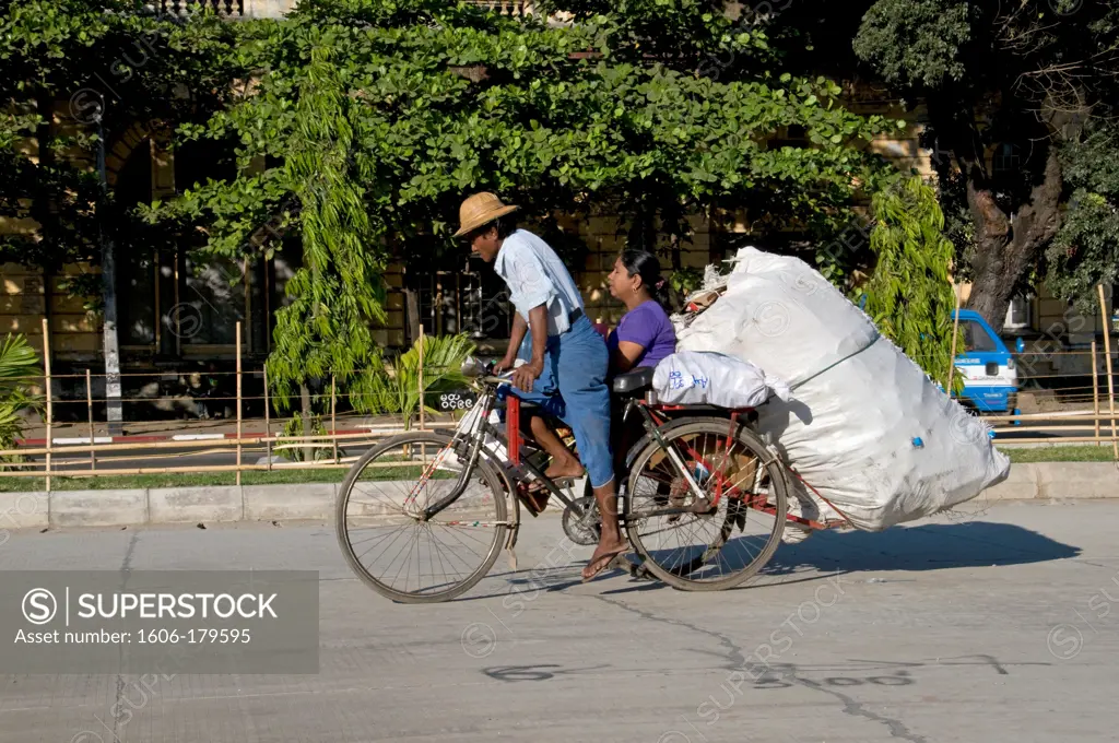 Myanmar Burma Yangon STRAND STREET a man riding a rickshaw is carrying a woman and a giant packet