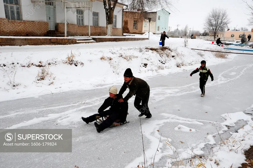 UZBEKISTAN KHIVA boys are playing with a sled on a frozen river