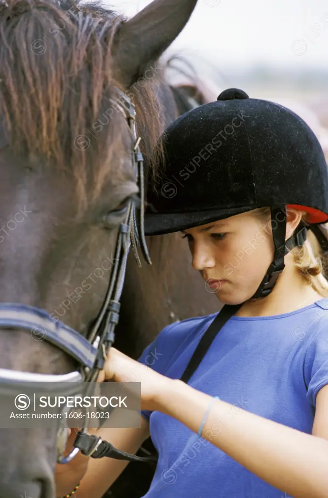 Portrait Jessica, bombe, tee-shirt bleu, harnachant cheval marron, extérieur