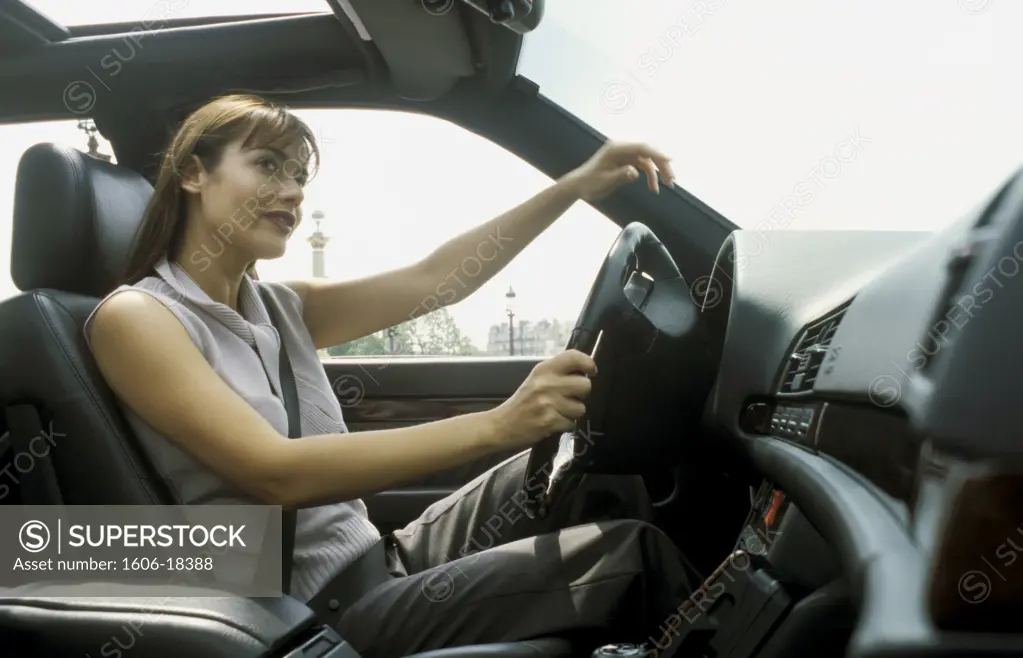 Woman sitting in her car, looking at rear-view mirror