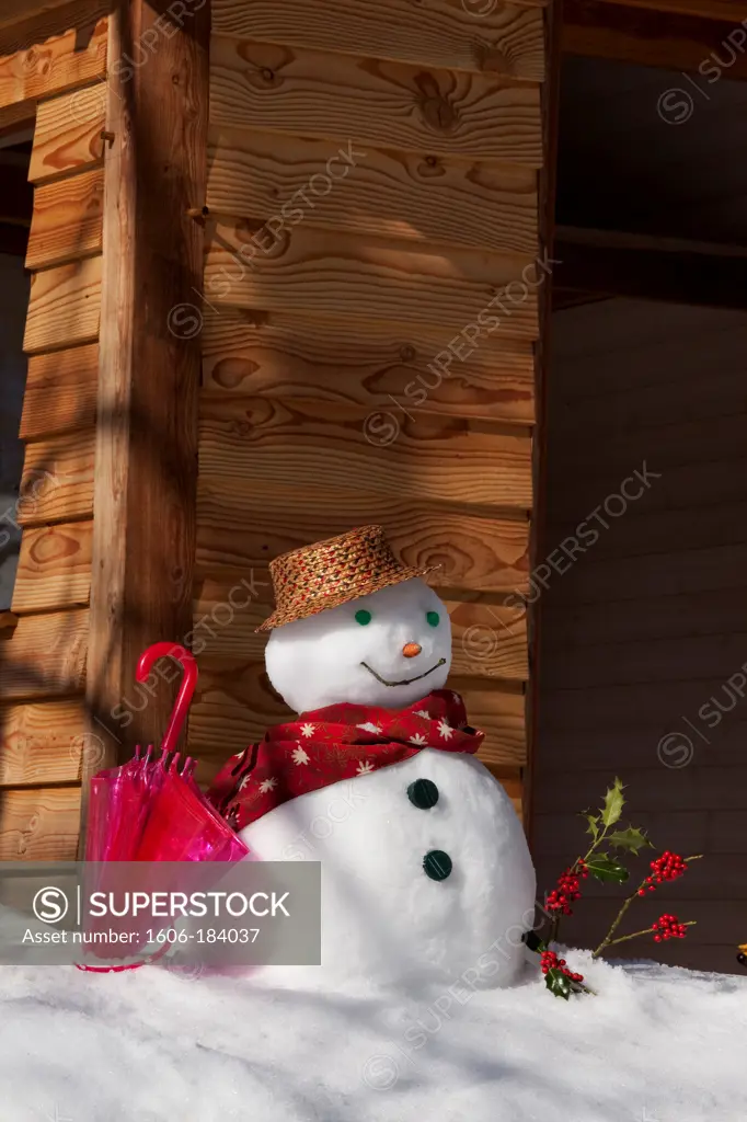 Snowman in front of a wooden house