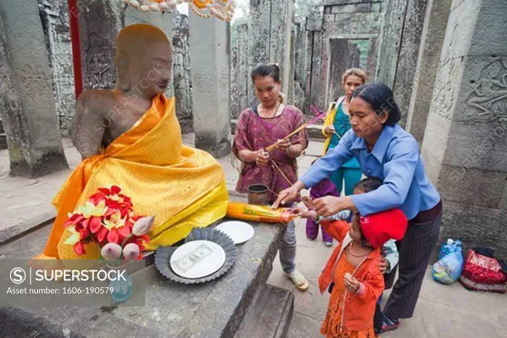 Cambodia, Siem Reap, Angkor Thom, Bayon Temple, Women and Children Preying to Buddha Statue