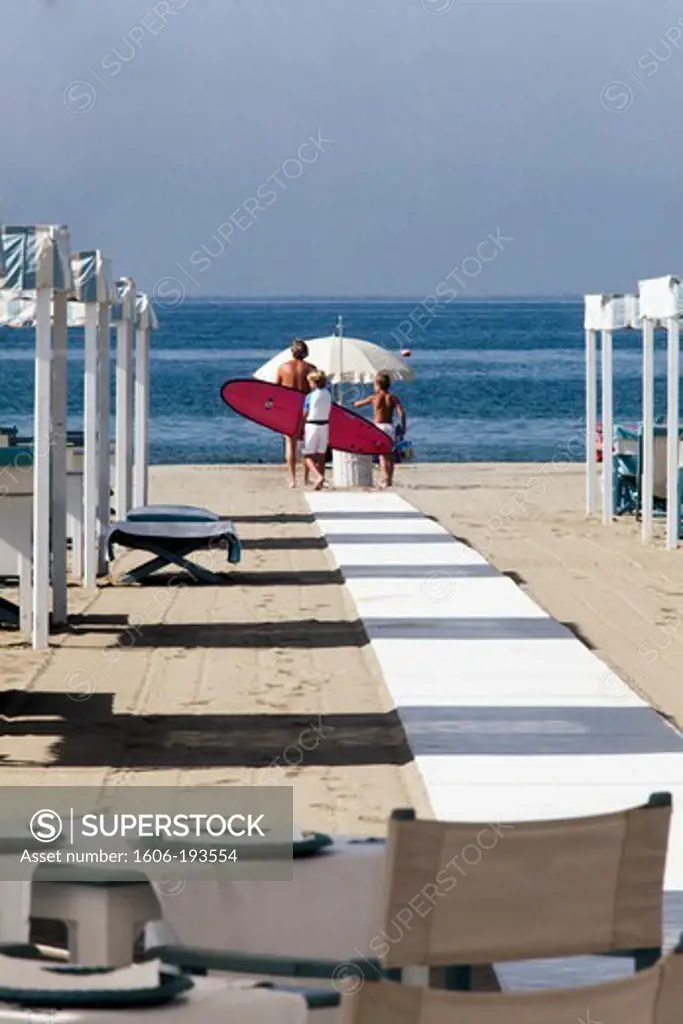 Italy, Forte Dei Marmi, Private Beach, A Father And His Sons Walking On The Beach With A Red Surf Board