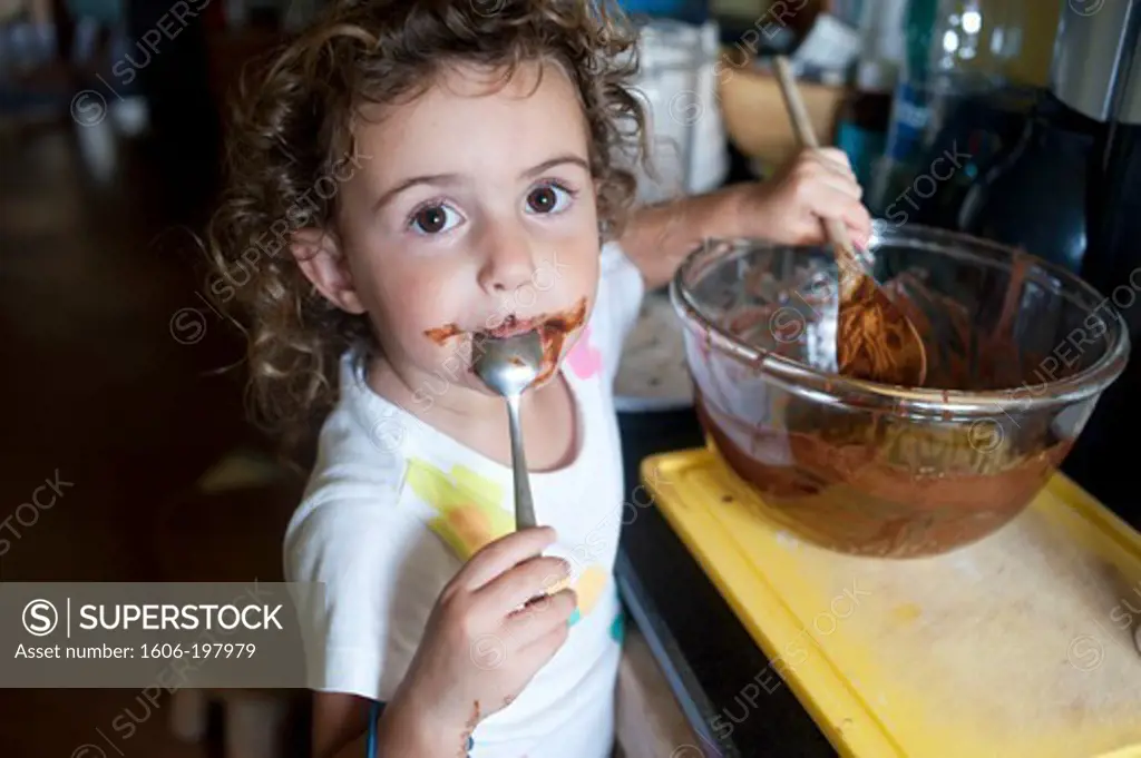 Young Girl Licking Chocolate Spoons In A Kitchen
