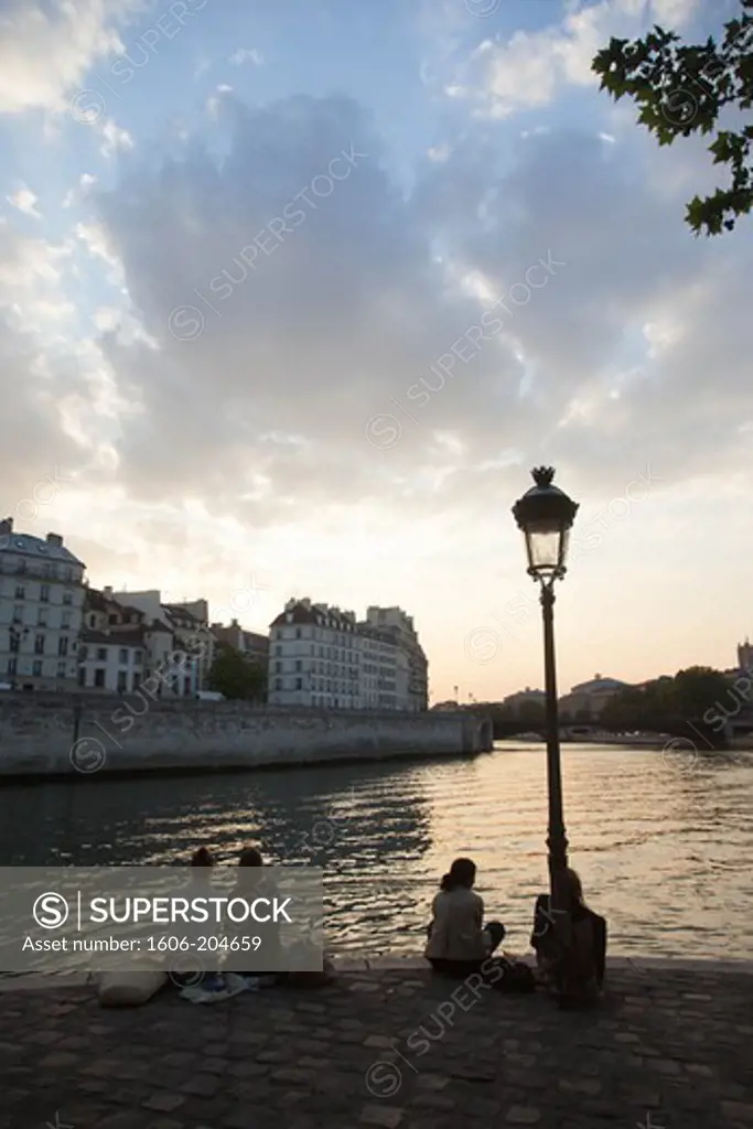 France, Paris, Île Saint Louis, People sitting on the quay at dusk,