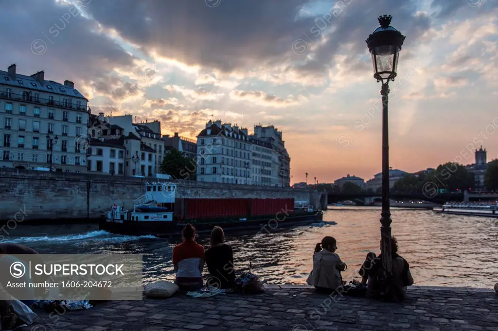 France, Paris, Île Saint Louis, People sitting on the quay at dusk