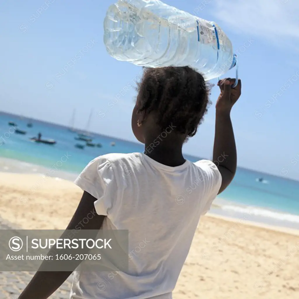 Western Africa,Republic of Cape Verde, Sal island. Santa Maria. Young girl with water bottle on her head.