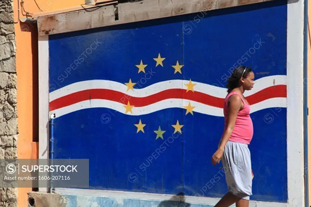 Western Africa,Republic of Cape Verde, Sal island. Santa Maria.Pregnant woman walking in front of the national flag.