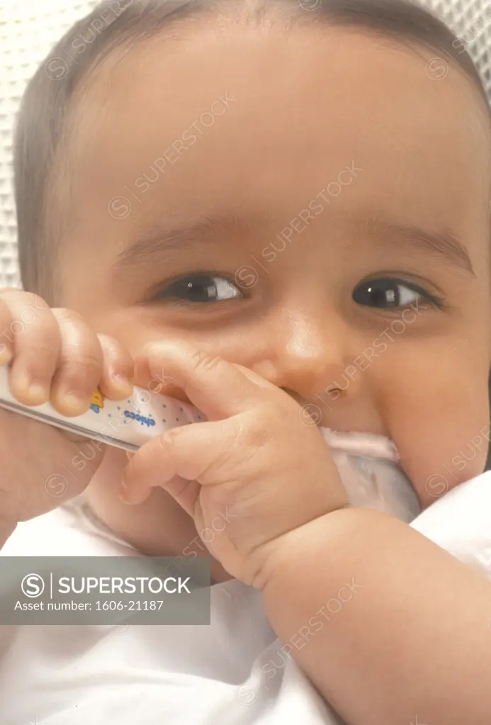 portrait d'un bébé de 7 mois, tenant à deux mains la cuillère de yaourt qu'il suce