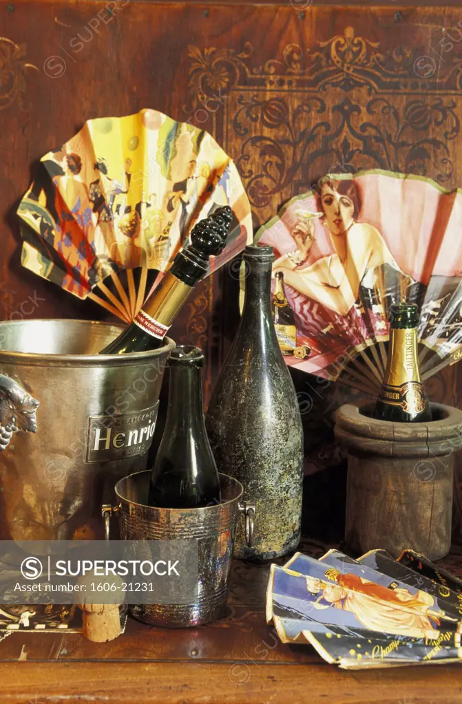 Composition 4  bouteilles, 2 seaux à champagne et 3 éventails sur table, mur en bois gravé en arrière-plan
