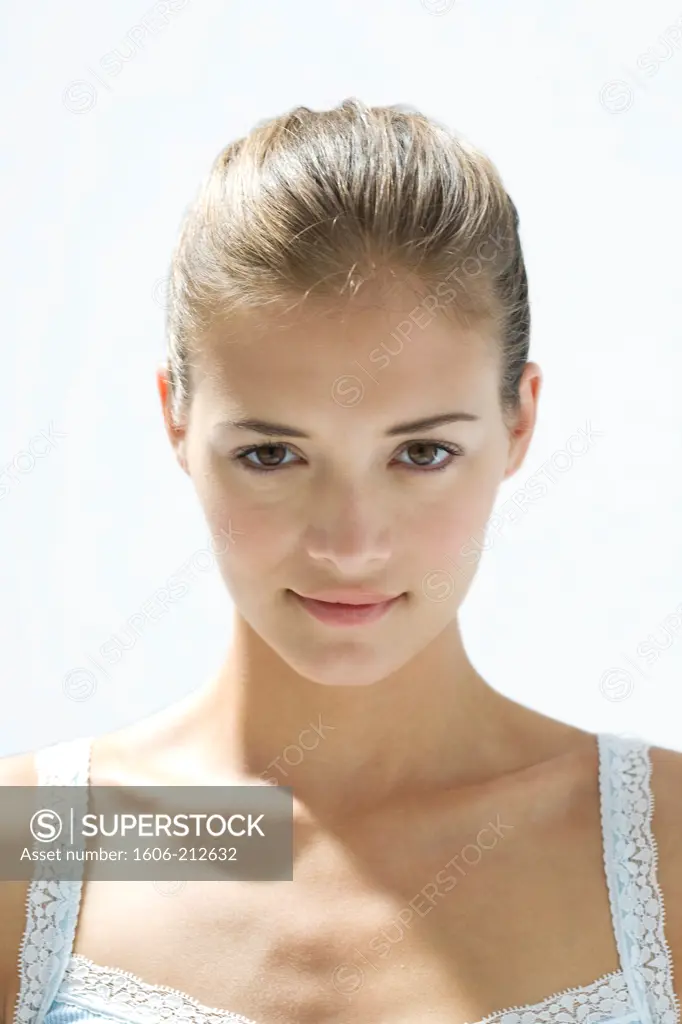 Portrait of a young woman face looking at camera, smirk, hair tied.