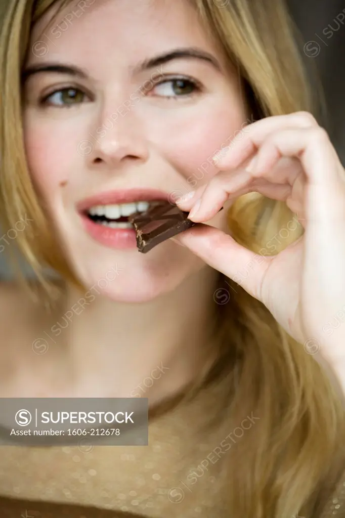 Close-up of a young woman eating a piece of chocolat bar.
