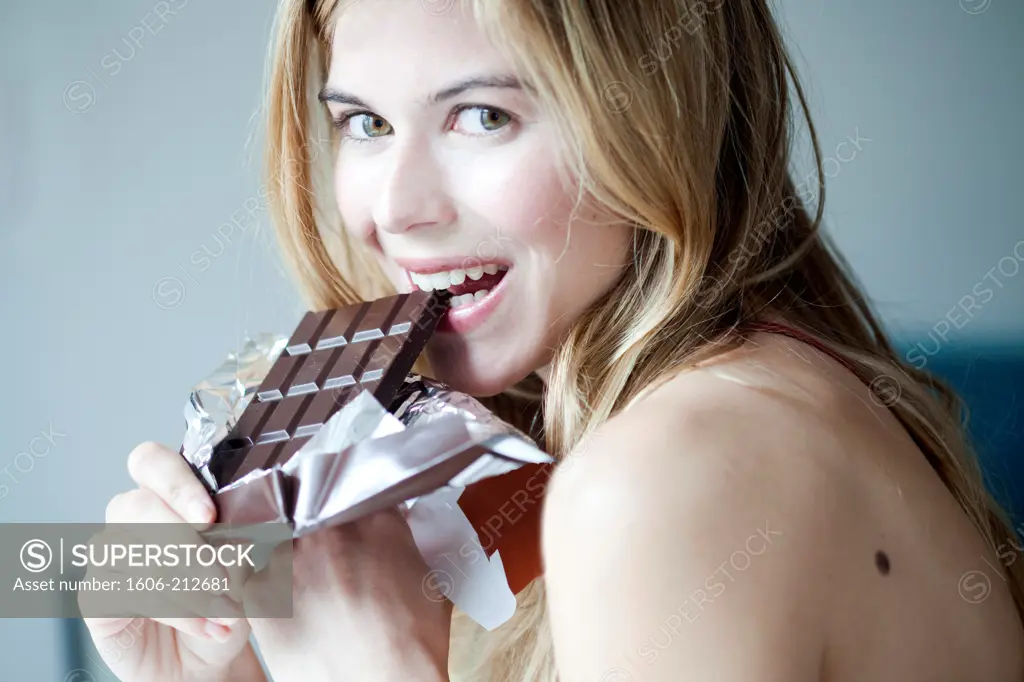 Portrait of a young woman eating a chocolate bar.