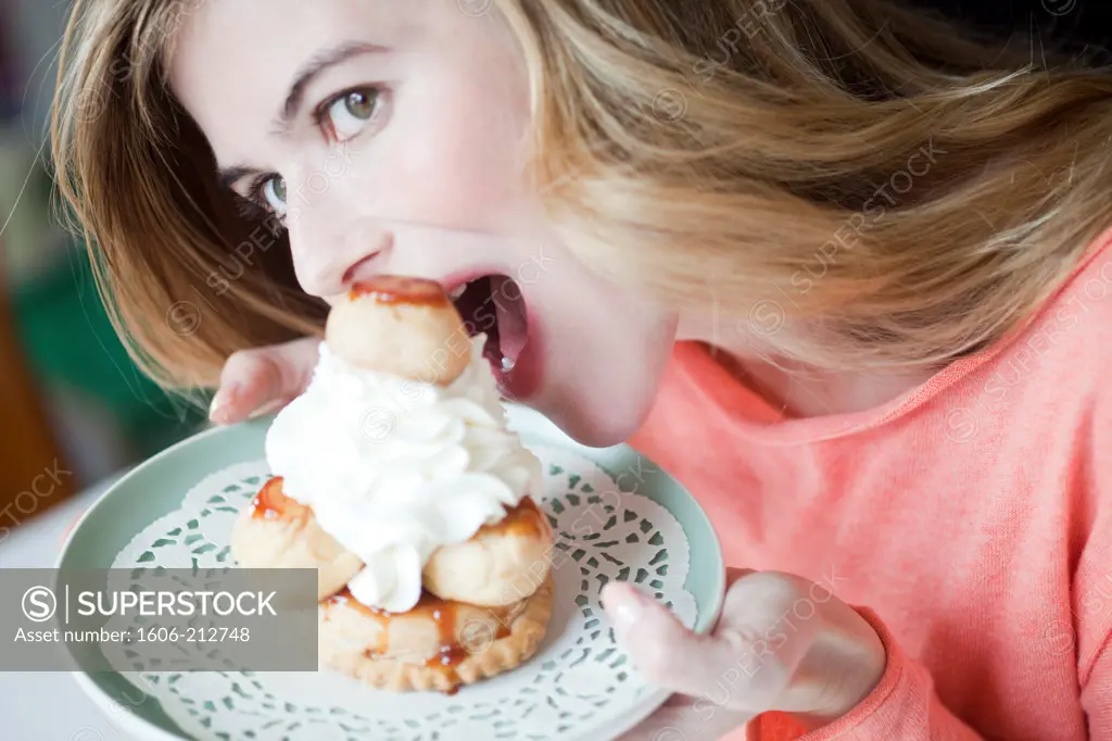 Portrait of a young woman eating cream puff and whipped cream pastry.