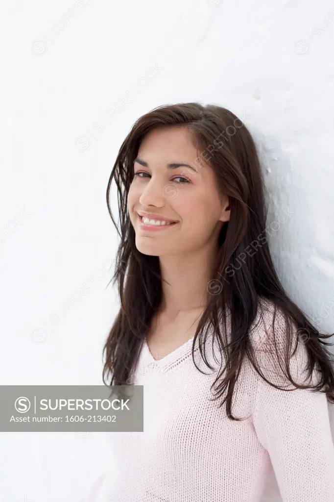 Portrait of a young woman leaning against a wall, smiling at camera