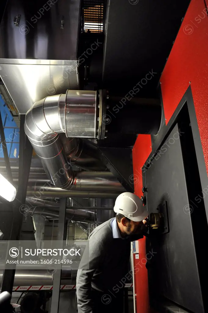 France, biomass boiler room supplied with wood waste for district heating in Nantes, technician checking the combustion
