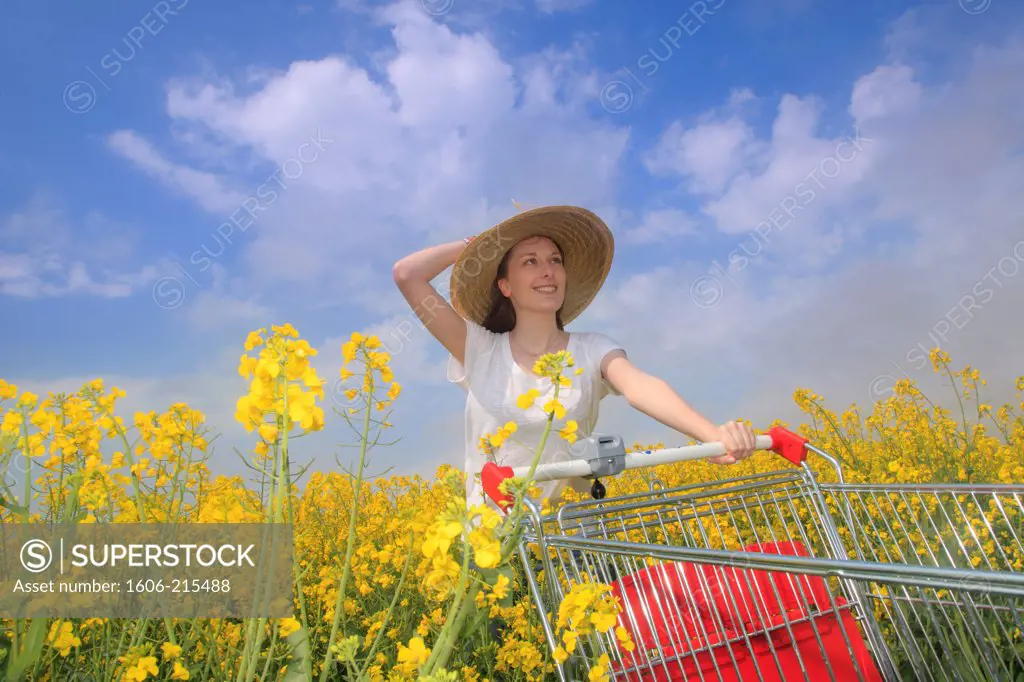 France, young woman in colza field with shopping trolley.
