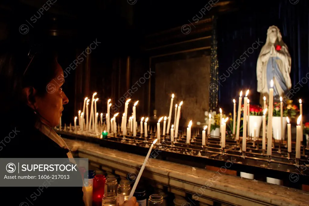 Woman lighting a candle in La Madeleine church. Paris. France.