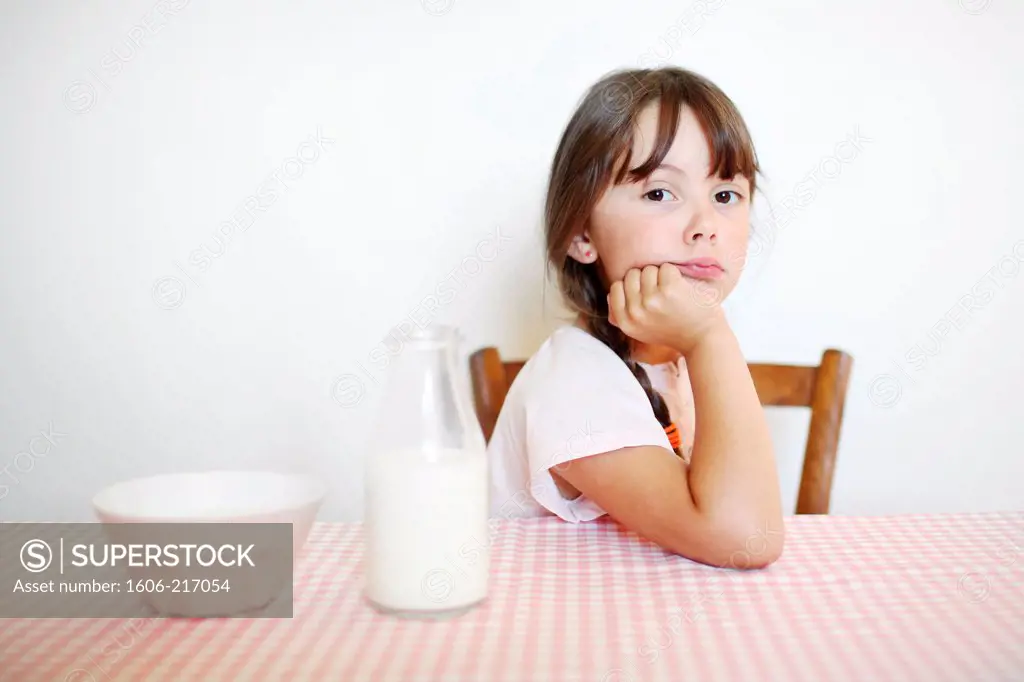 A little girl sitting at her breakfast table with a bowl of milk.